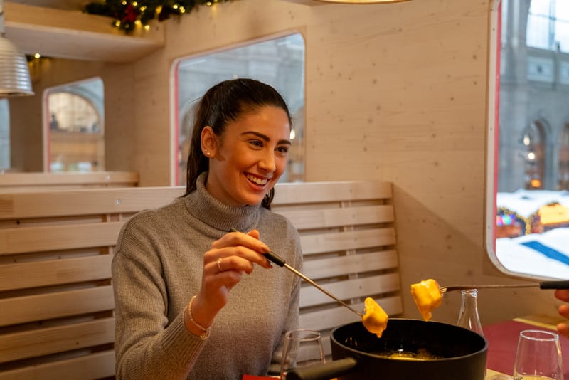 Gast taucht Brot in das Fondue im Polarzauber Parsennbahn Fondue-Express