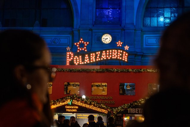 Der leuchtende Polarzauber-Schriftzug über dem Wagen des Fondue-Express, im Vordergrund Besuchende.