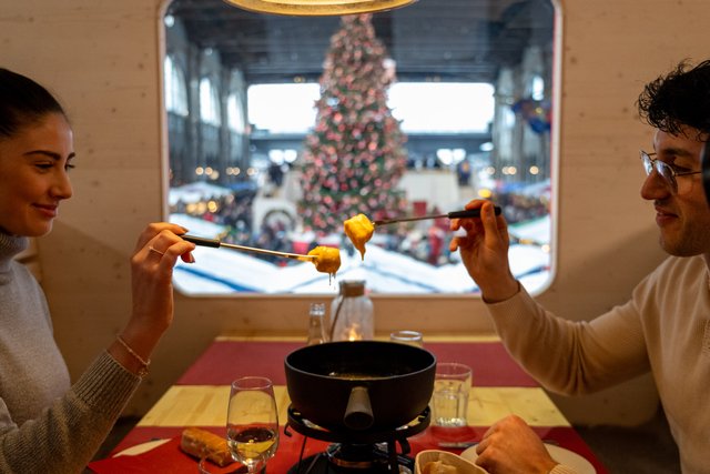 Fondue im Parsennbahn Fondue-Express, durchs Fenster der Weihnachtsbaum in der Halle.