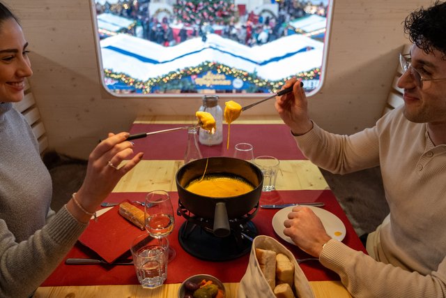Zwei Gäste beim Fondue im Fondue-Express, im Fenster das Markttreiben.